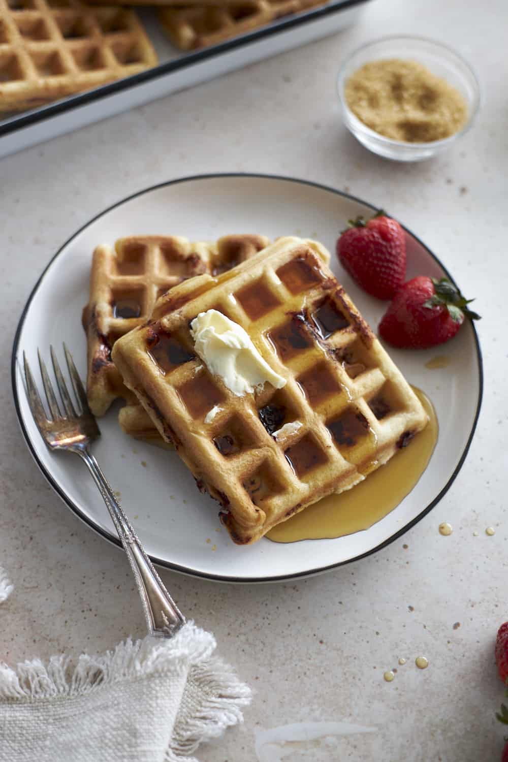 Two waffles on a white plate with butter and maple syrup.