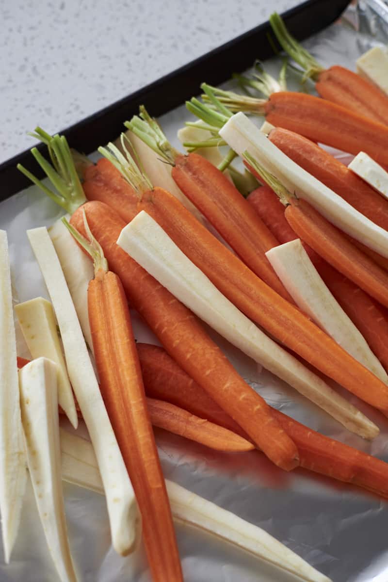 Raw carrots and parsnips on a baking sheet.