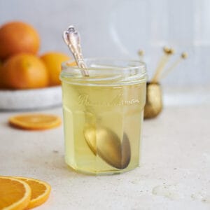 Orange simple syrup in a glass jar with a spoon.