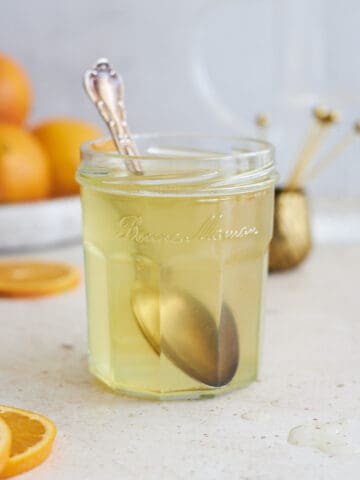 Orange simple syrup in a glass jar with a spoon.