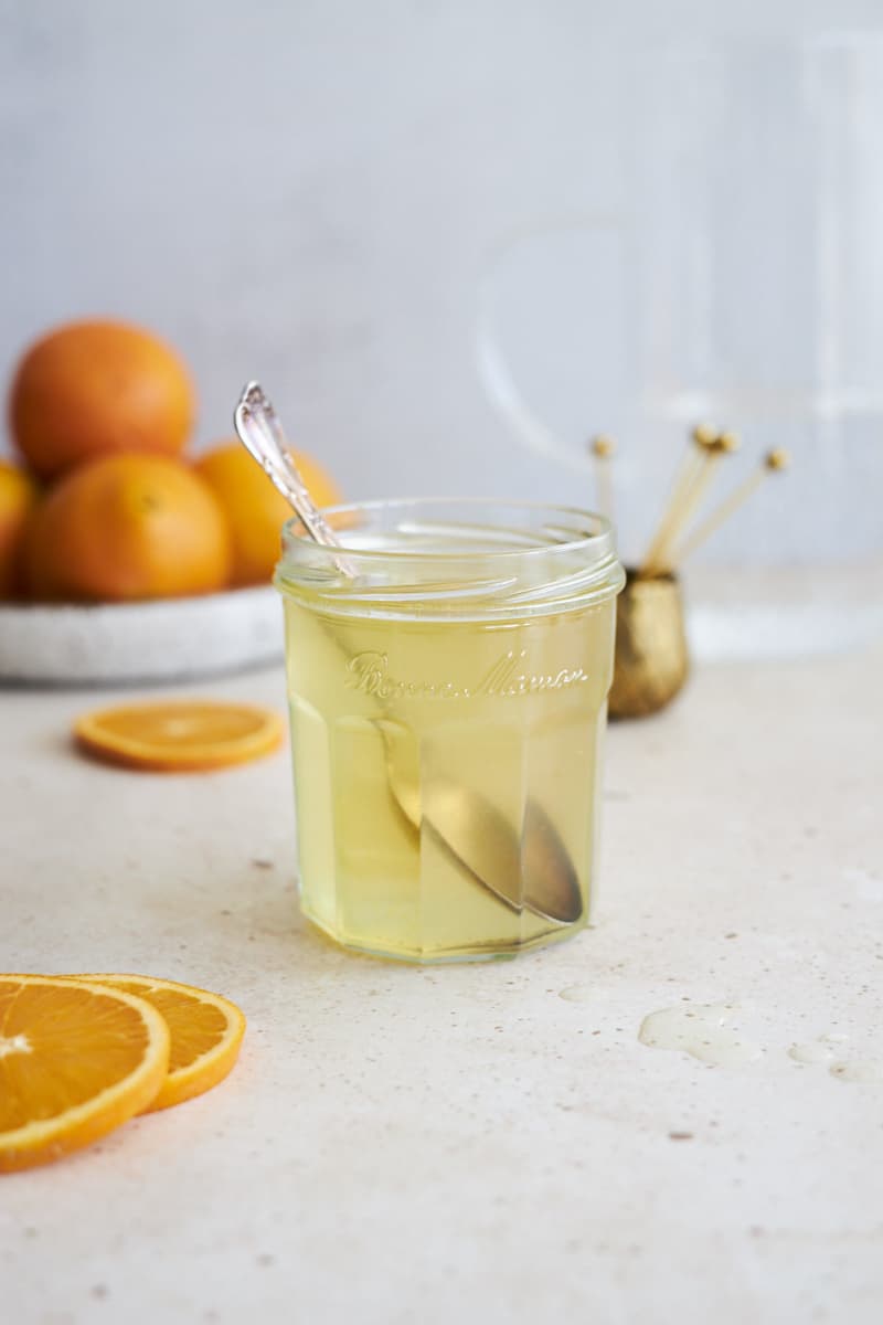 Orange simple syrup in a glass jar with a spoon.