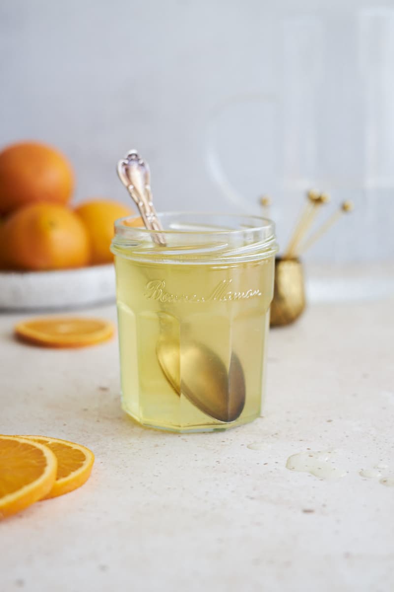 Orange simple syrup in a glass jar with a spoon.