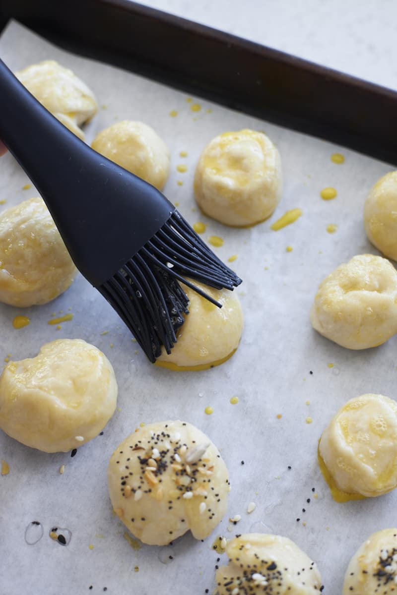 A black brush adding egg wash to the pretzel bites.