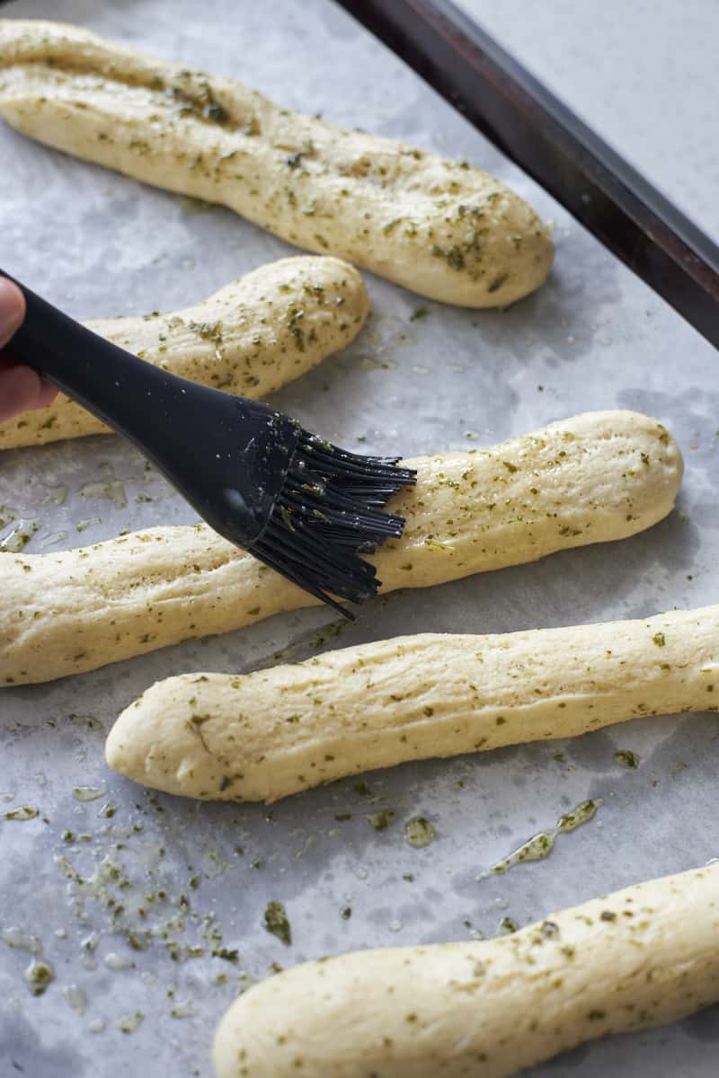 Brushing sourdough discard breadsticks with the garlic butter mixture.