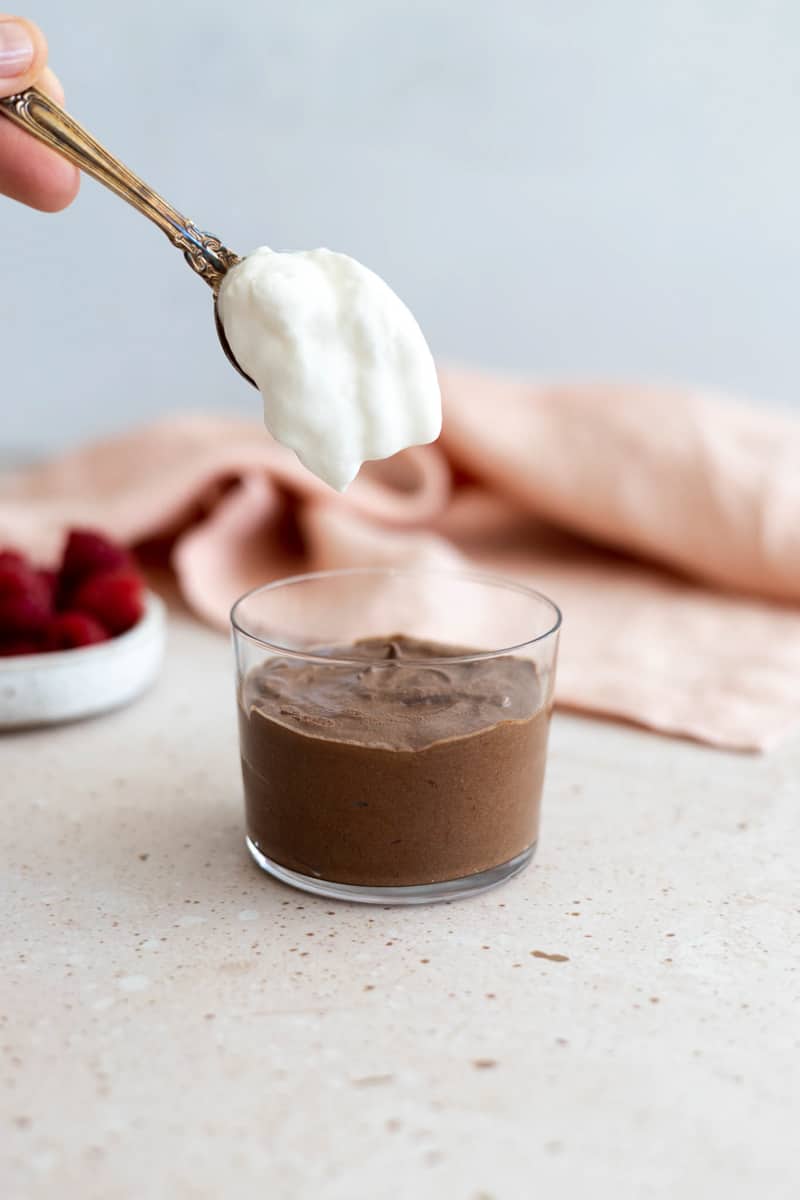 A spoon adding whipped cream to the chocolate mousse.