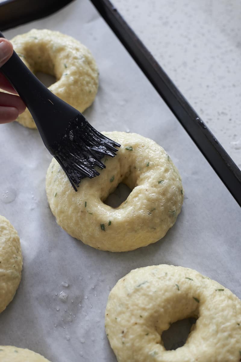 Bagels being brushed with egg wash.