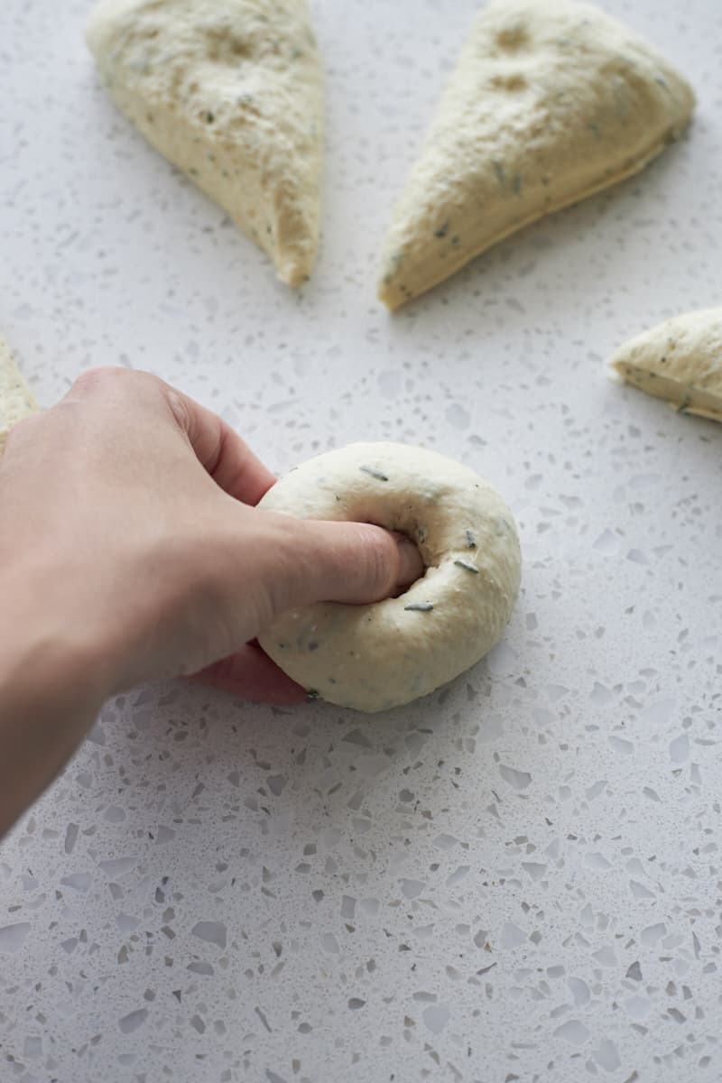 Thumb pressing a hole in the center of the bagel dough.