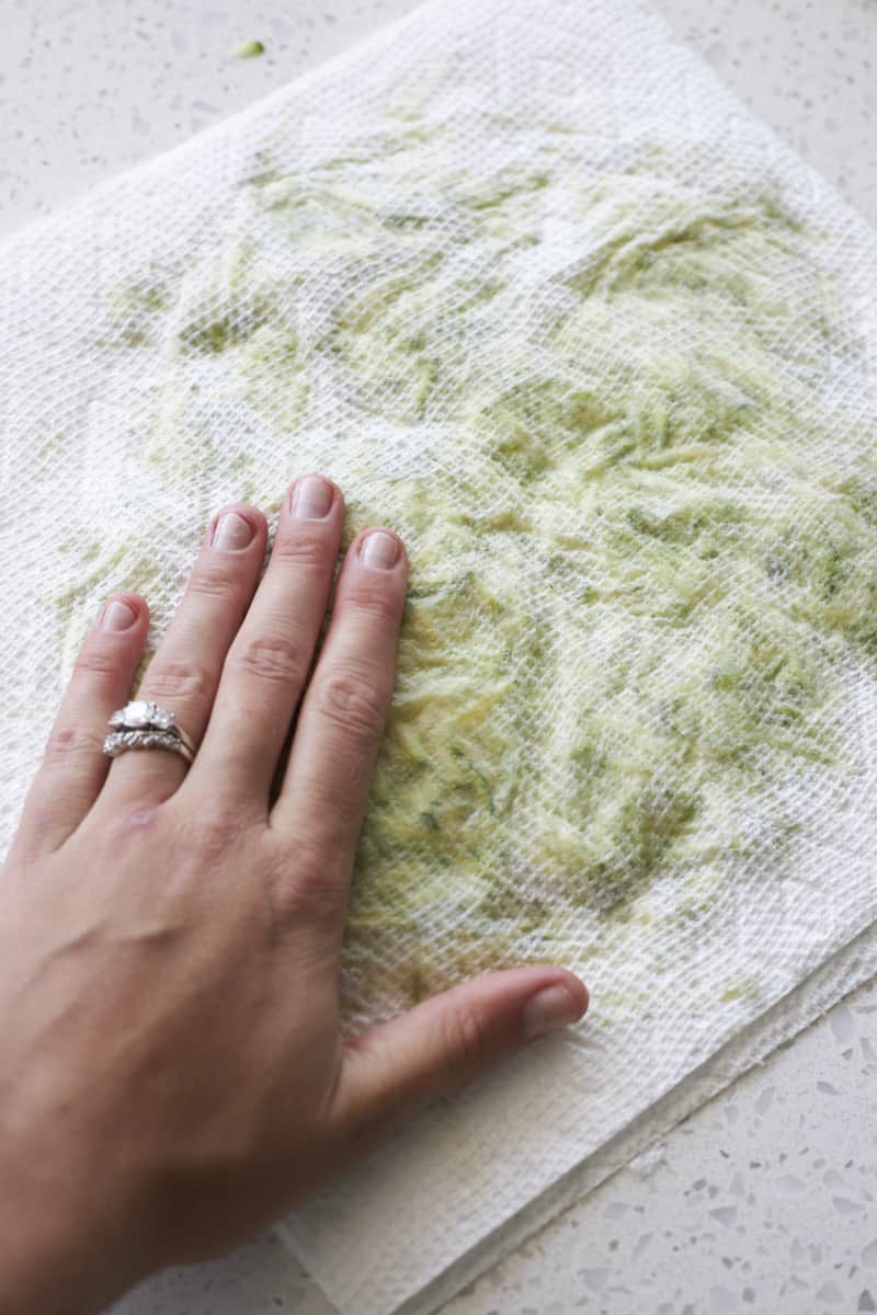 Shredded zucchini being pressed between two layers of paper towels. 