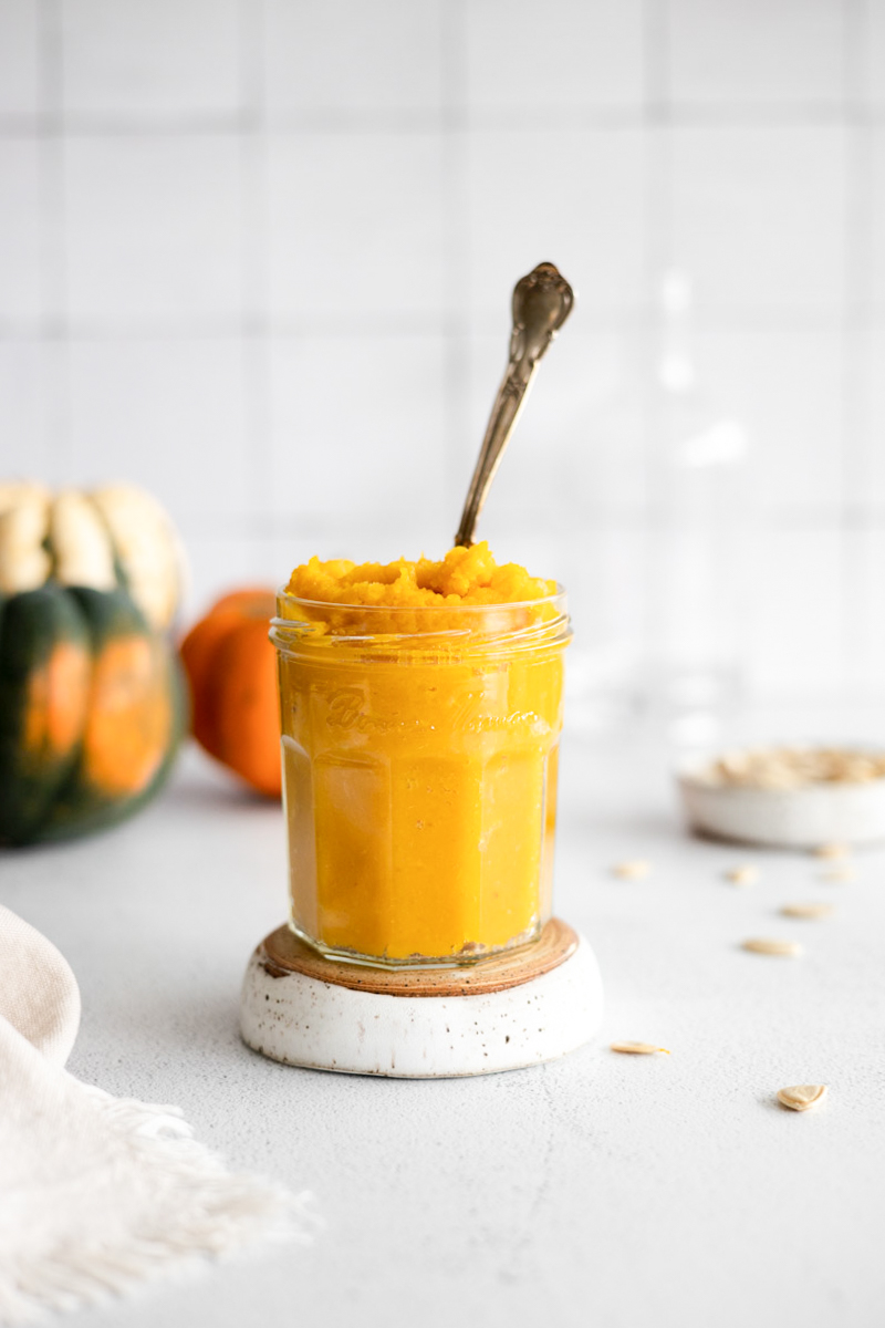 Homemade pumpkin purée in a jar with a spoon.