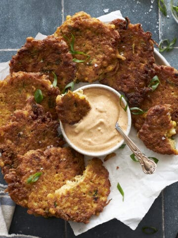 Zucchini and Sweetcorn Fritters on a platter with aioli dipping sauce.