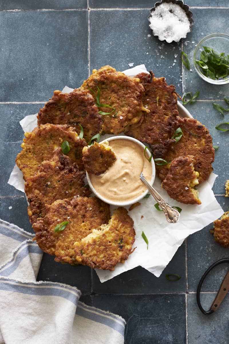 Zucchini and Sweetcorn Fritters on a round platter with aioli dipping sauce.