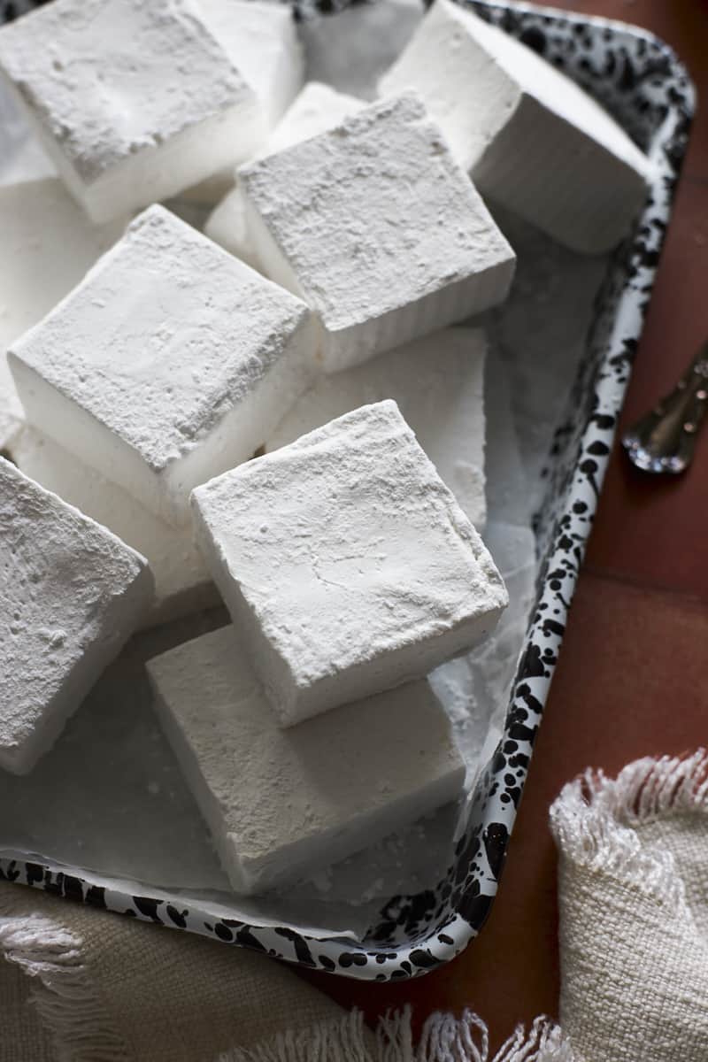 Marshmallows in a pile on a black and white speckled tray.