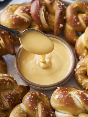 A spoonful of Honey Mustard Dipping Sauce with a platter of soft pretzels.