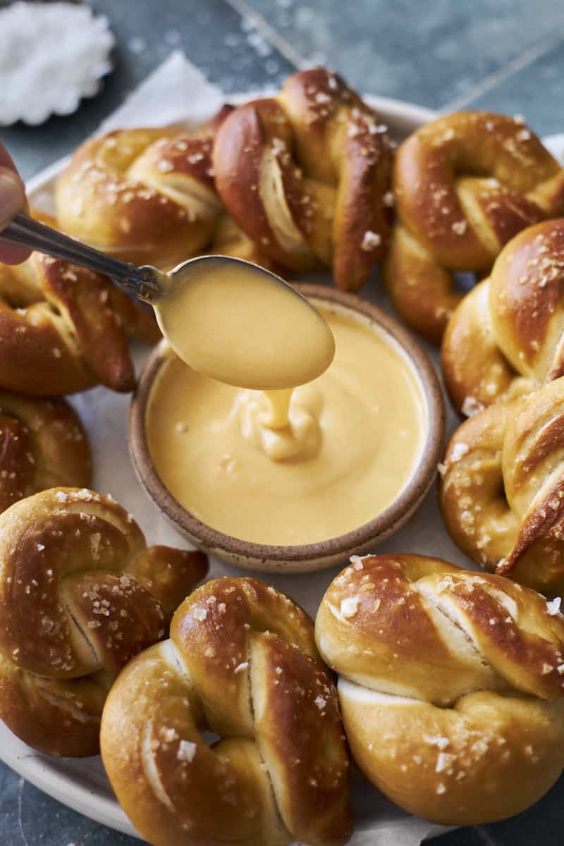 A spoonful of Honey Mustard Dipping Sauce with a platter of soft pretzels.