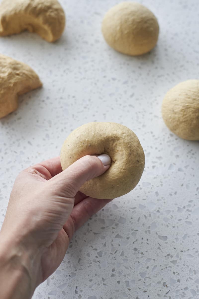 A thumb pressing a hole in the center of the bagel dough.