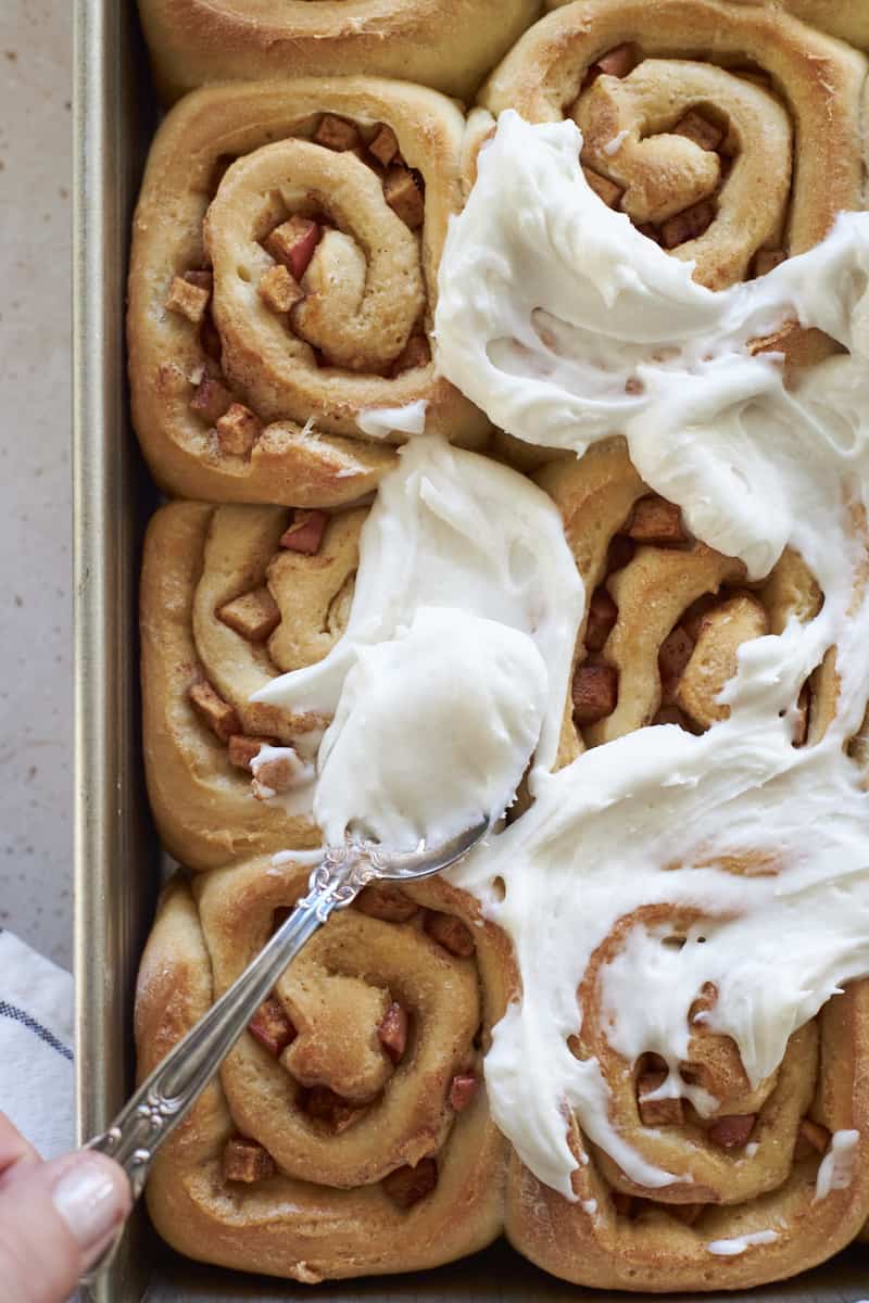 A spoon spreading frosting on the cinnamon rolls.