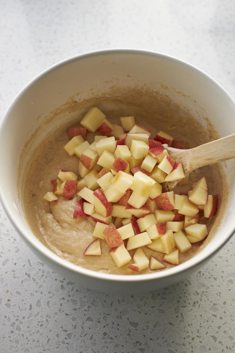 Apples being folded into the batter in a large bowl.