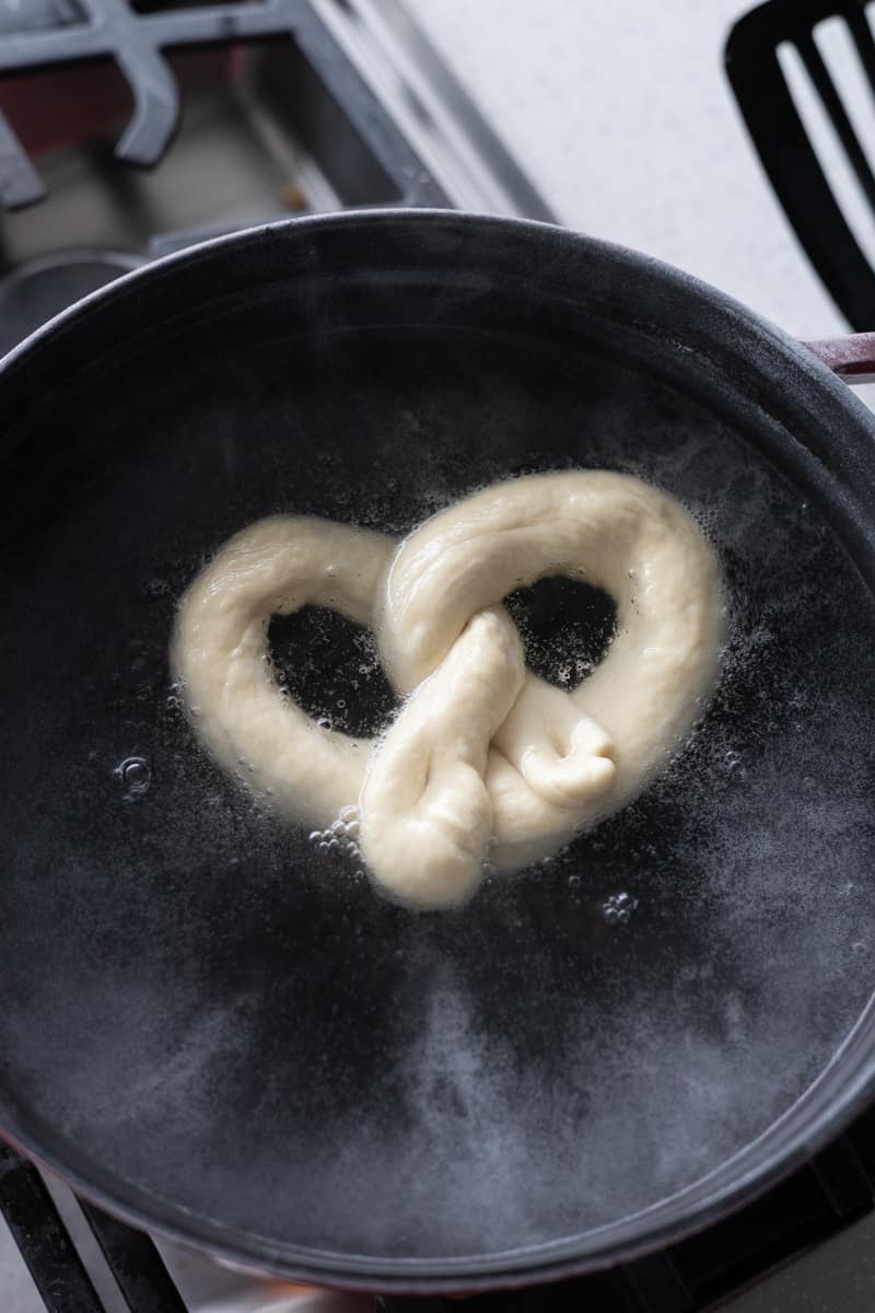 Pretzel floating in pot of boiling water.