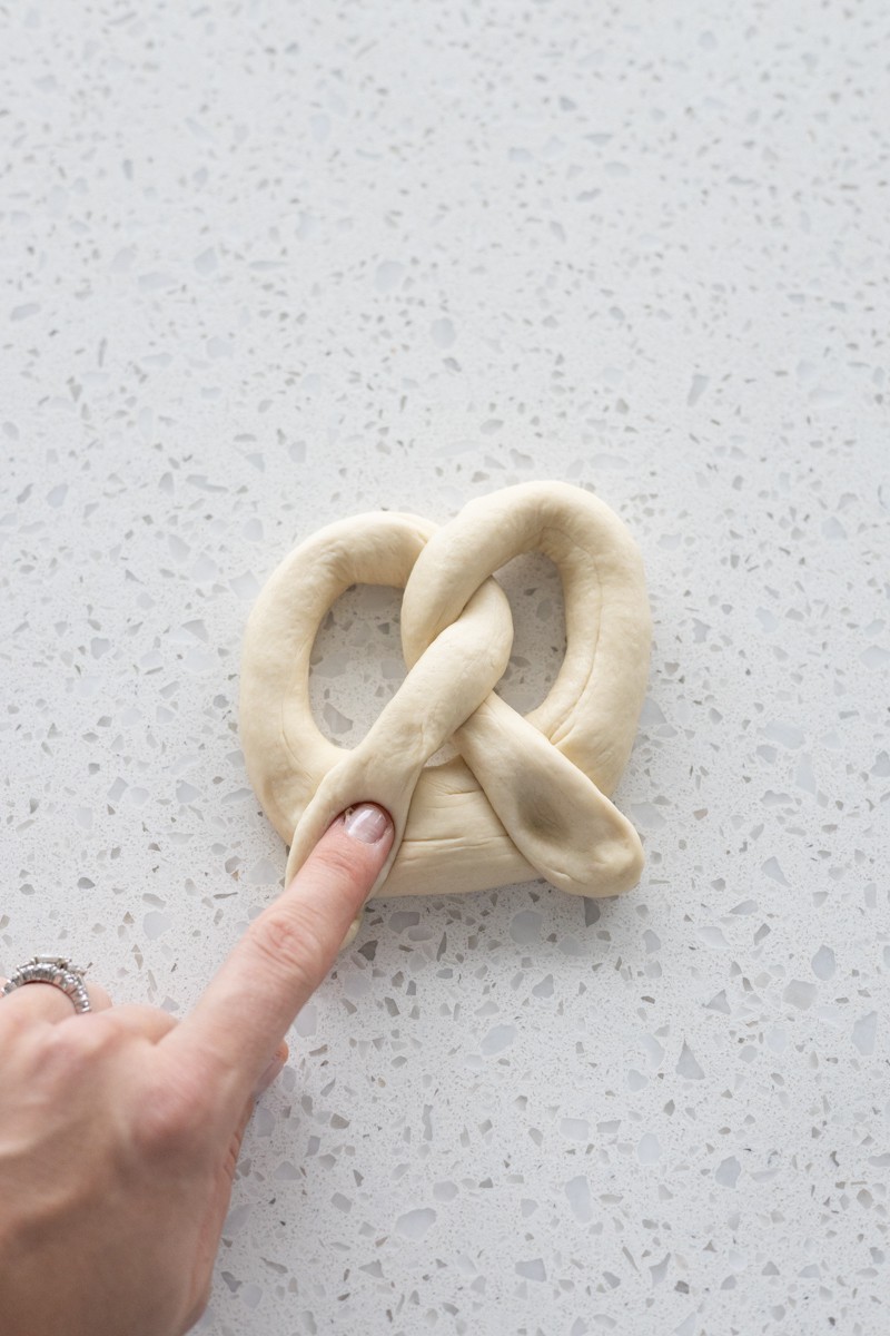 A finger pressing the end of the dough into the bottom of the pretzel shape.