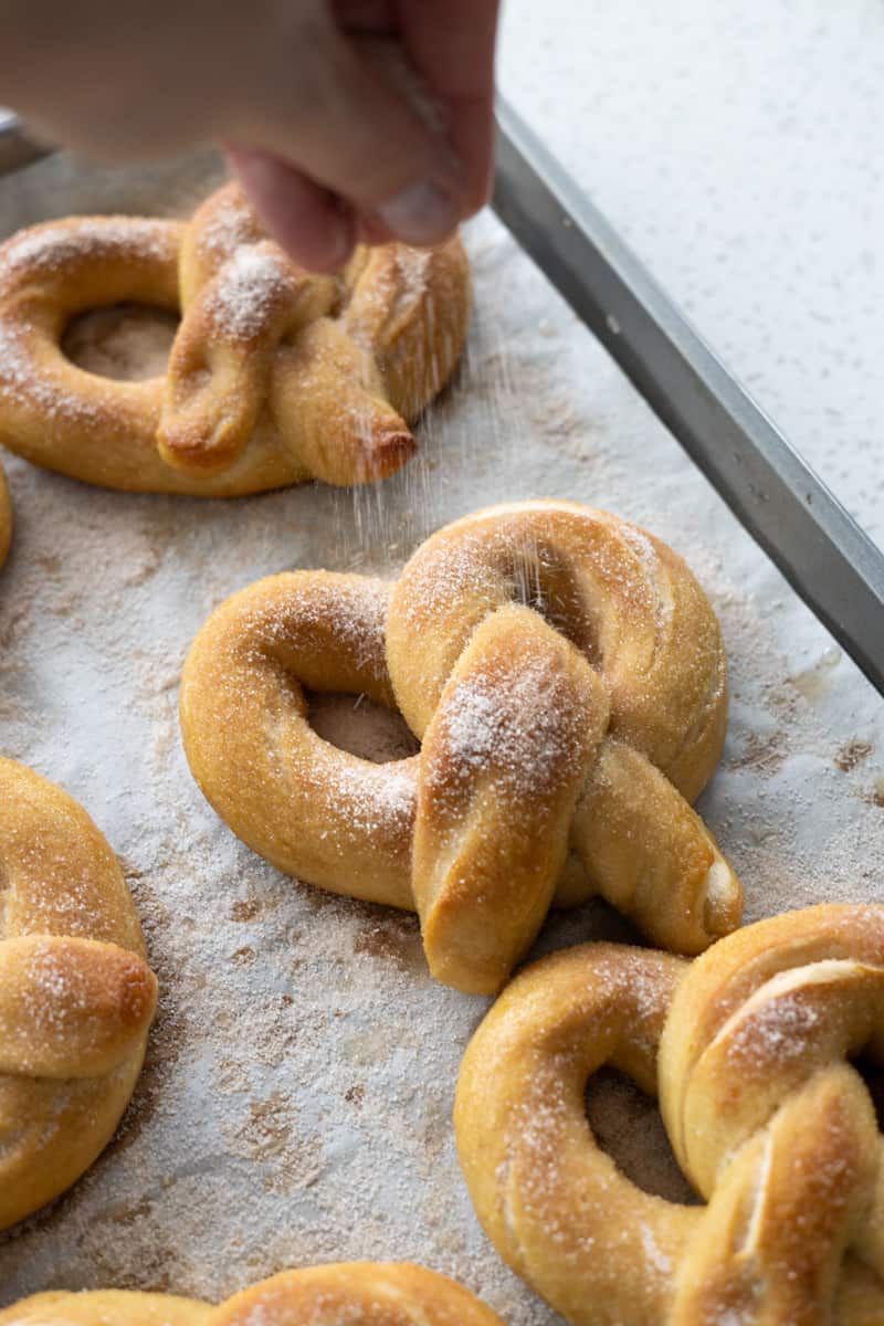 A pretzel being sprinkled with cinnamon sugar mixture.