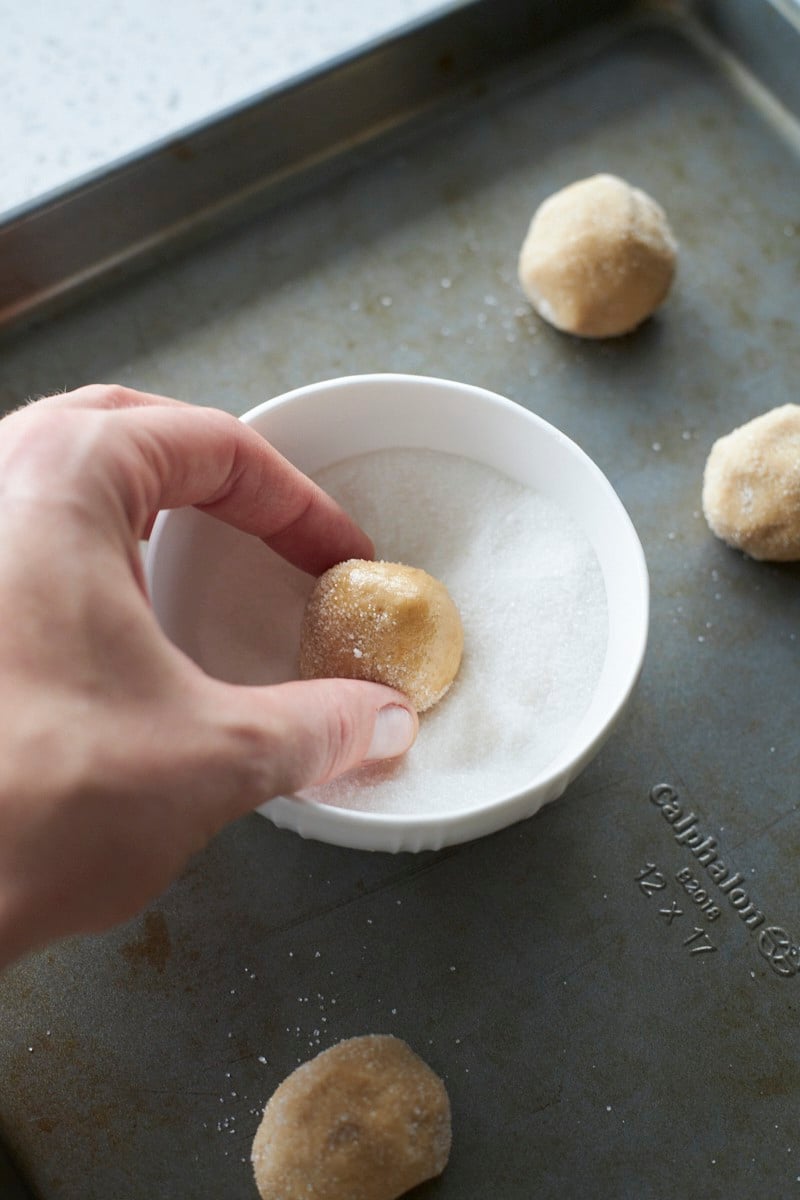 A hand rolling the dough ball in a small bowl of sugar.