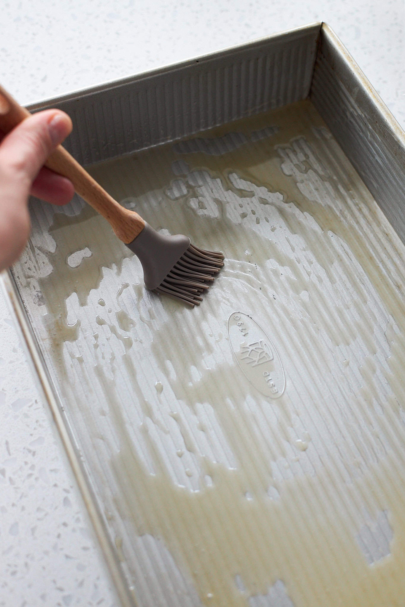 Brushing the 9x13-inch baking pan with melted butter.