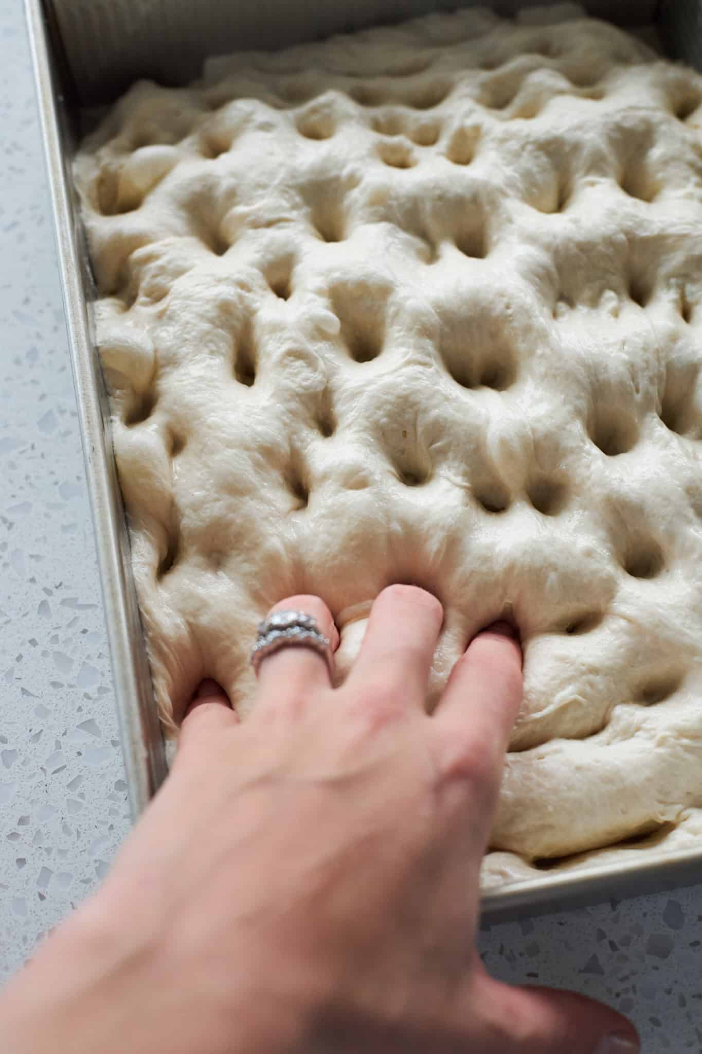 A hand poking dimples in the dough.