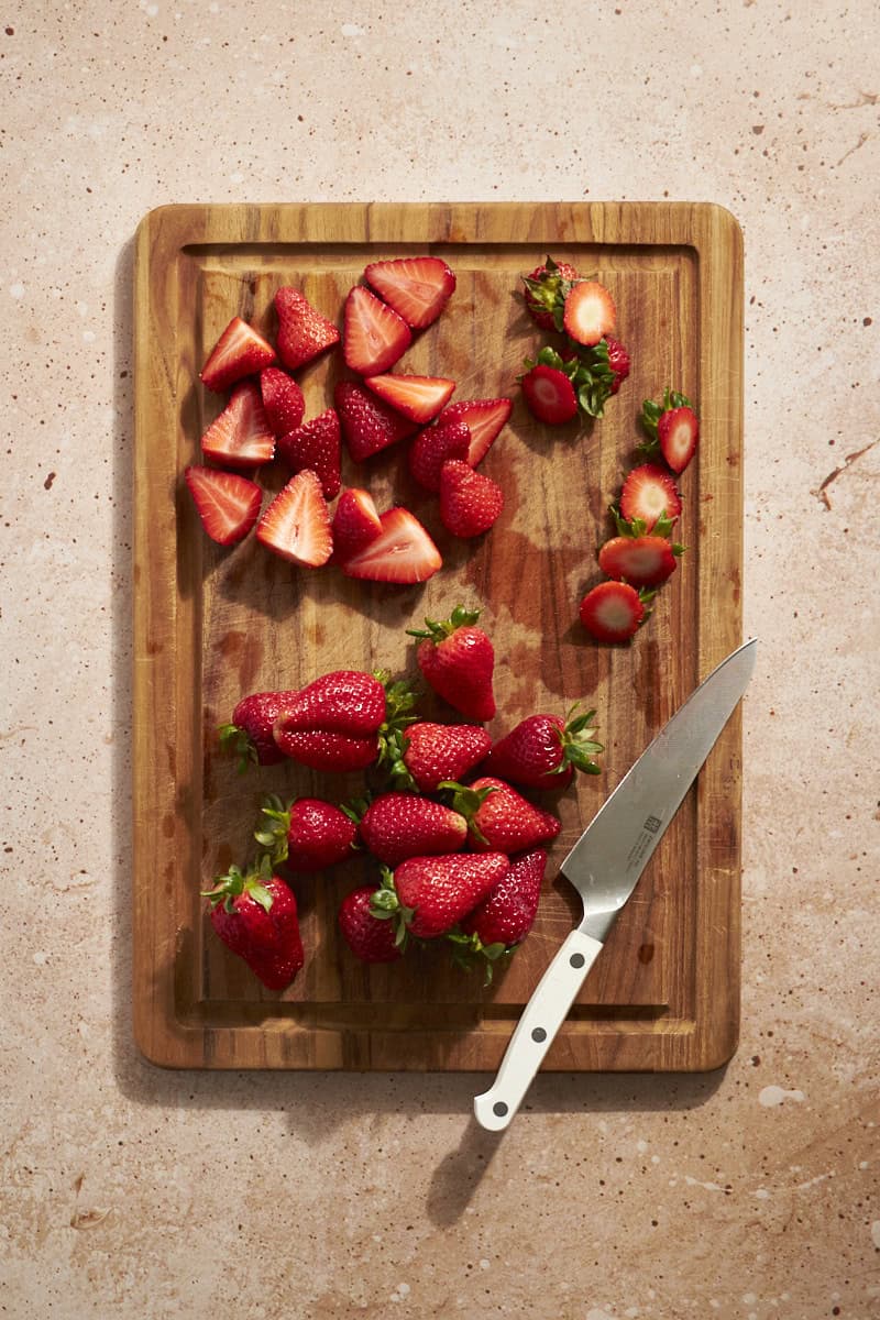 Strawberries sliced on a wooden cutting board.