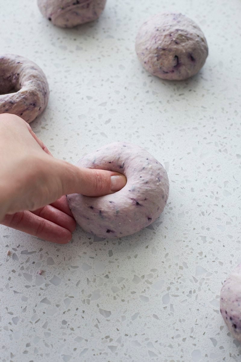 A thumb pressing a hole in the center of a bagel.