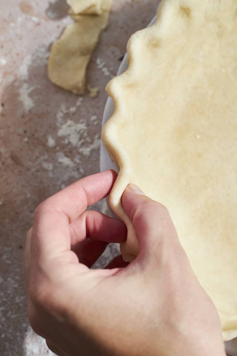 A hand crimping the edges of the pie crust.