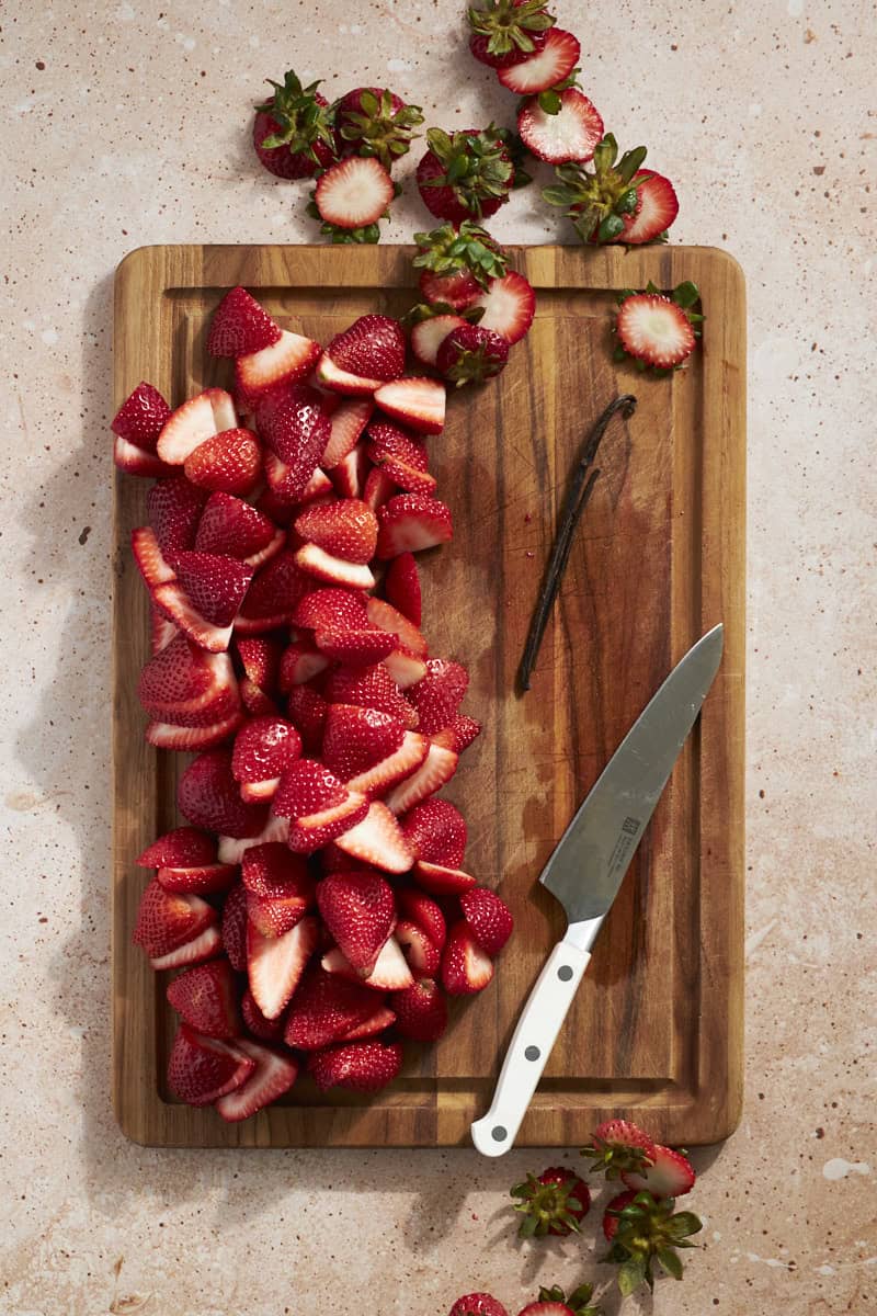 Strawberries sliced on a wooden cutting board.