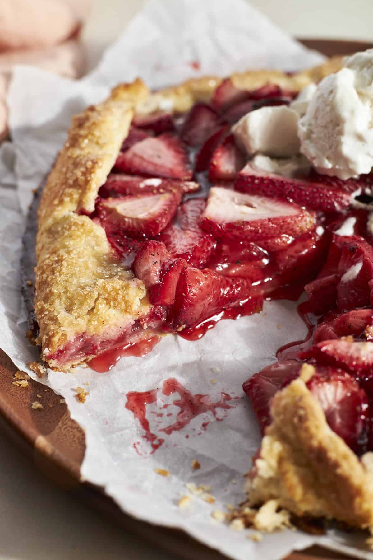 A slice of Sourdough Discard Strawberry Galette on white parchment paper with an ice cream topping. 