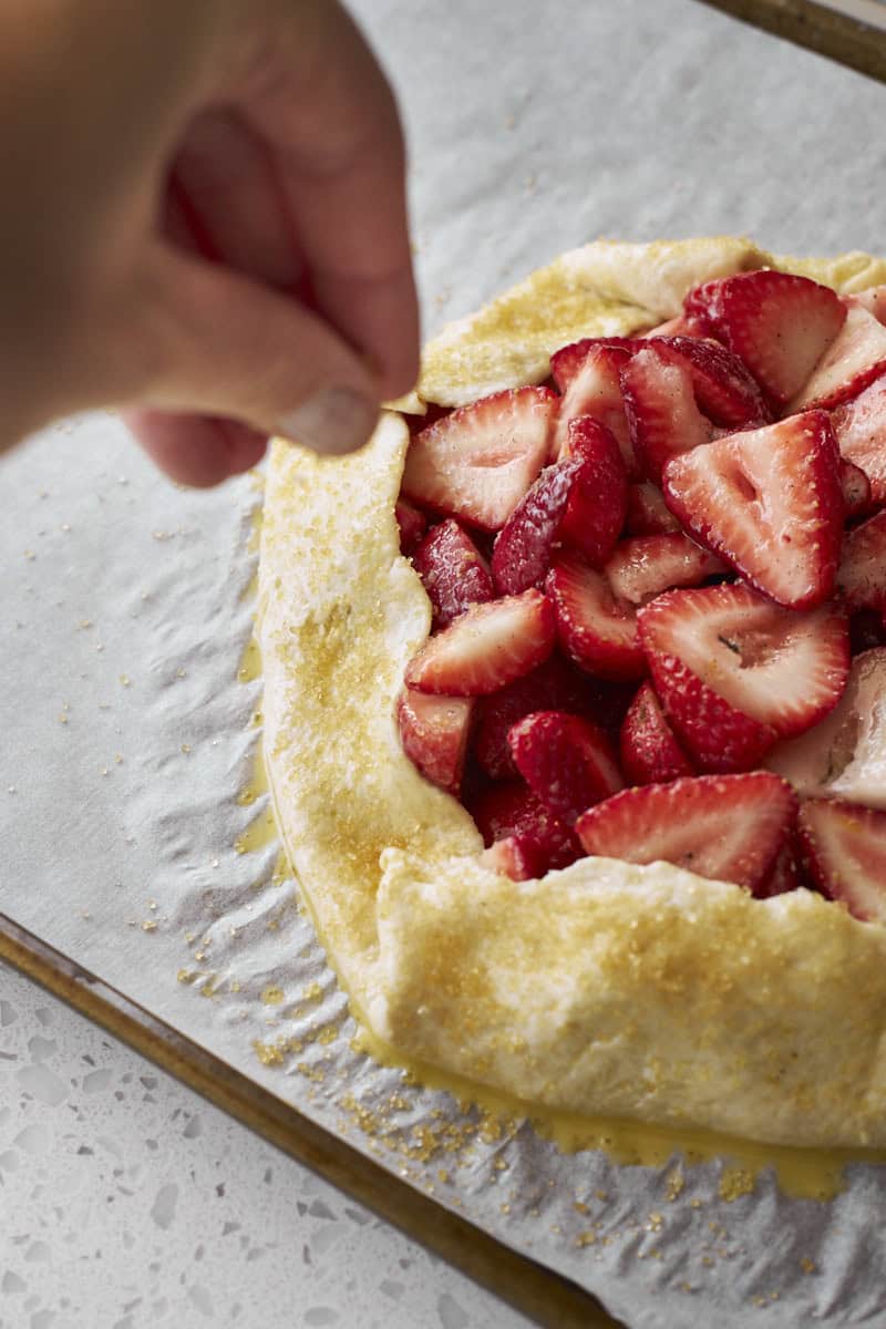 A hand sprinkling the galette with turbinado sugar.