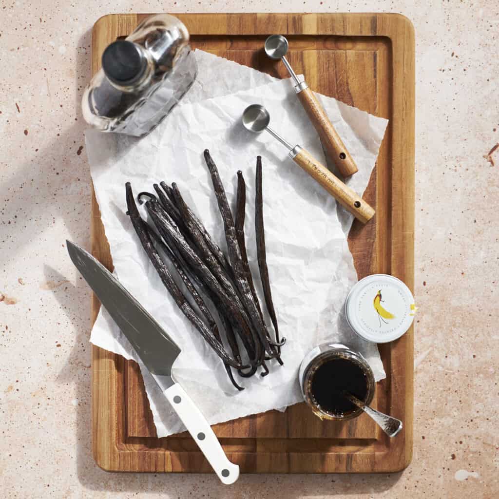 Vanilla extract, vanilla beans, and vanilla bean paste on a wooden cutting board.
