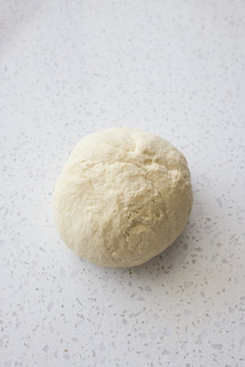 Dough kneaded into a ball on a work surface.