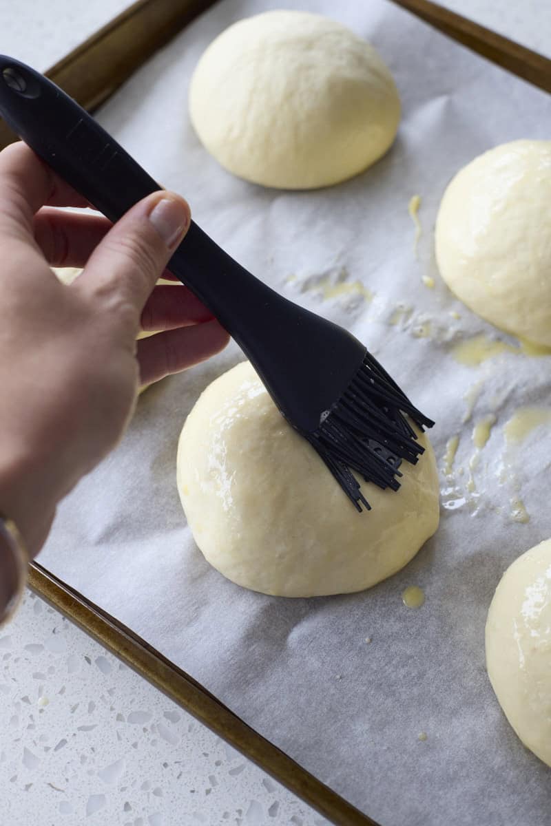 A hand brushing the buns with egg wash.