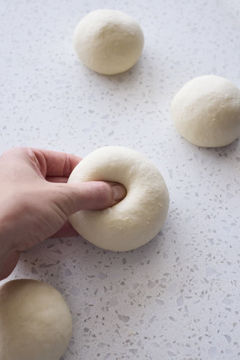 A thumb pressing a hole in the center of the bagel dough.