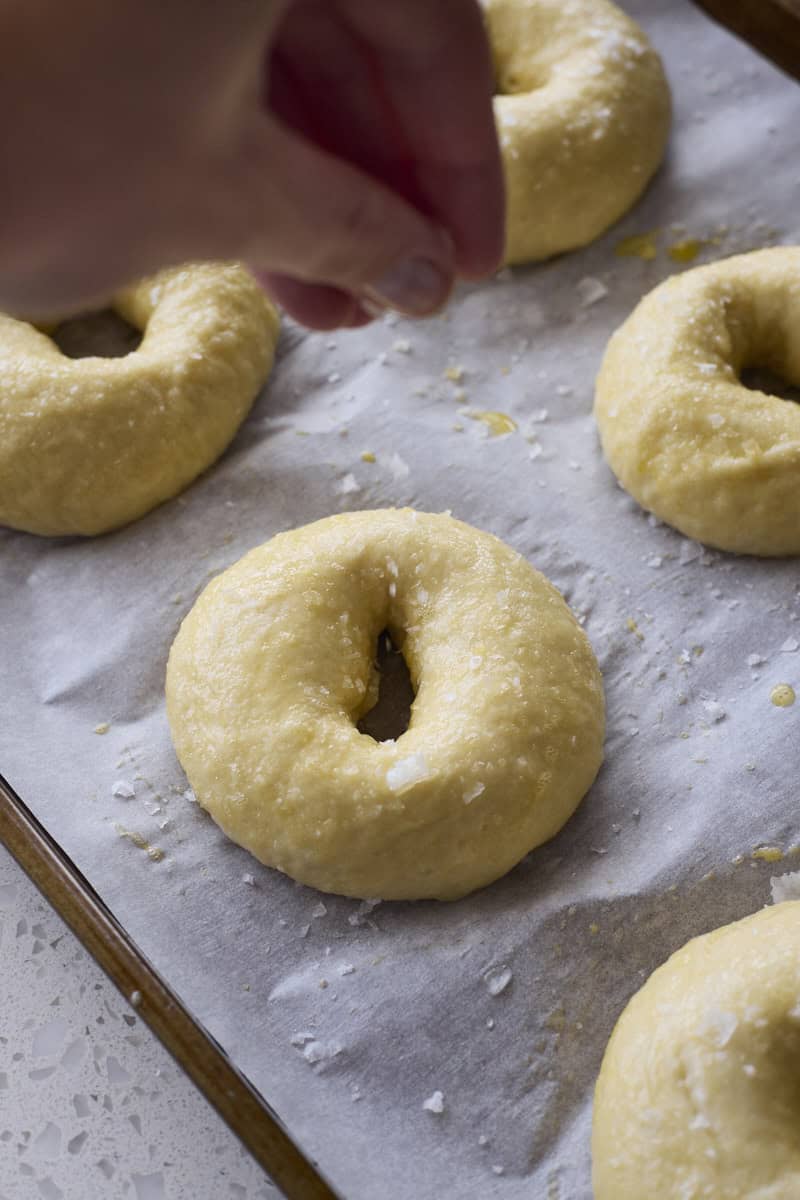A hand sprinkling salt on top of the bagels.