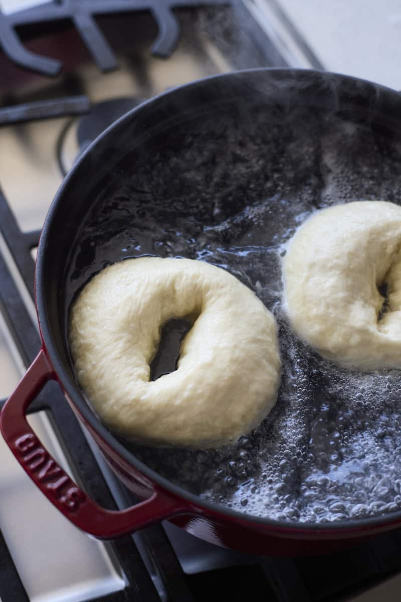 Bagels being boiled in a large pot of water.