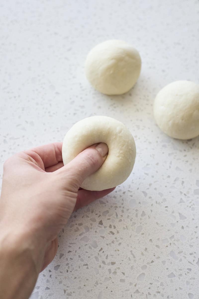 A thumb pressing the hole in the center of the bagel dough.