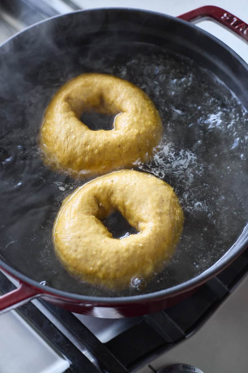 Bagels boiling in a large pot of water.
