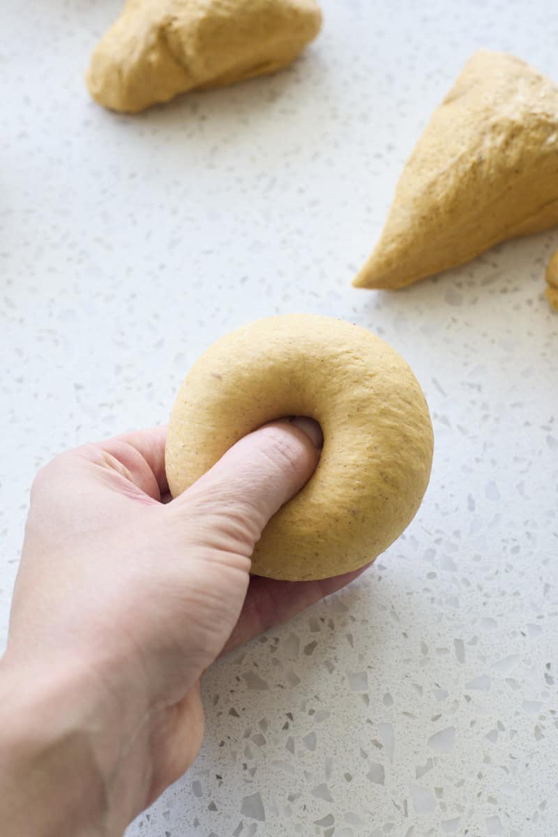 A hand pressing a hole in the center of the bagel.