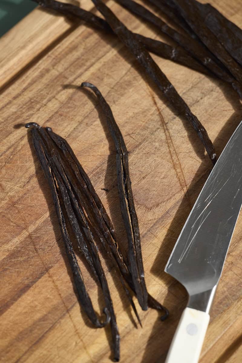 Vanilla beans cut in half on a wooden cutting board.