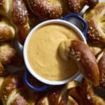 An overhead shot of Beer Cheese in a small bowl on a platter with soft pretzels.