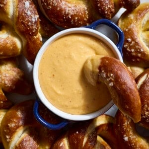 An overhead shot of Beer Cheese in a small bowl on a platter with soft pretzels.