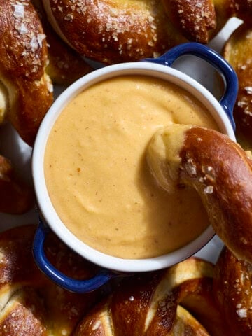 An overhead shot of Beer Cheese in a small bowl on a platter with soft pretzels.