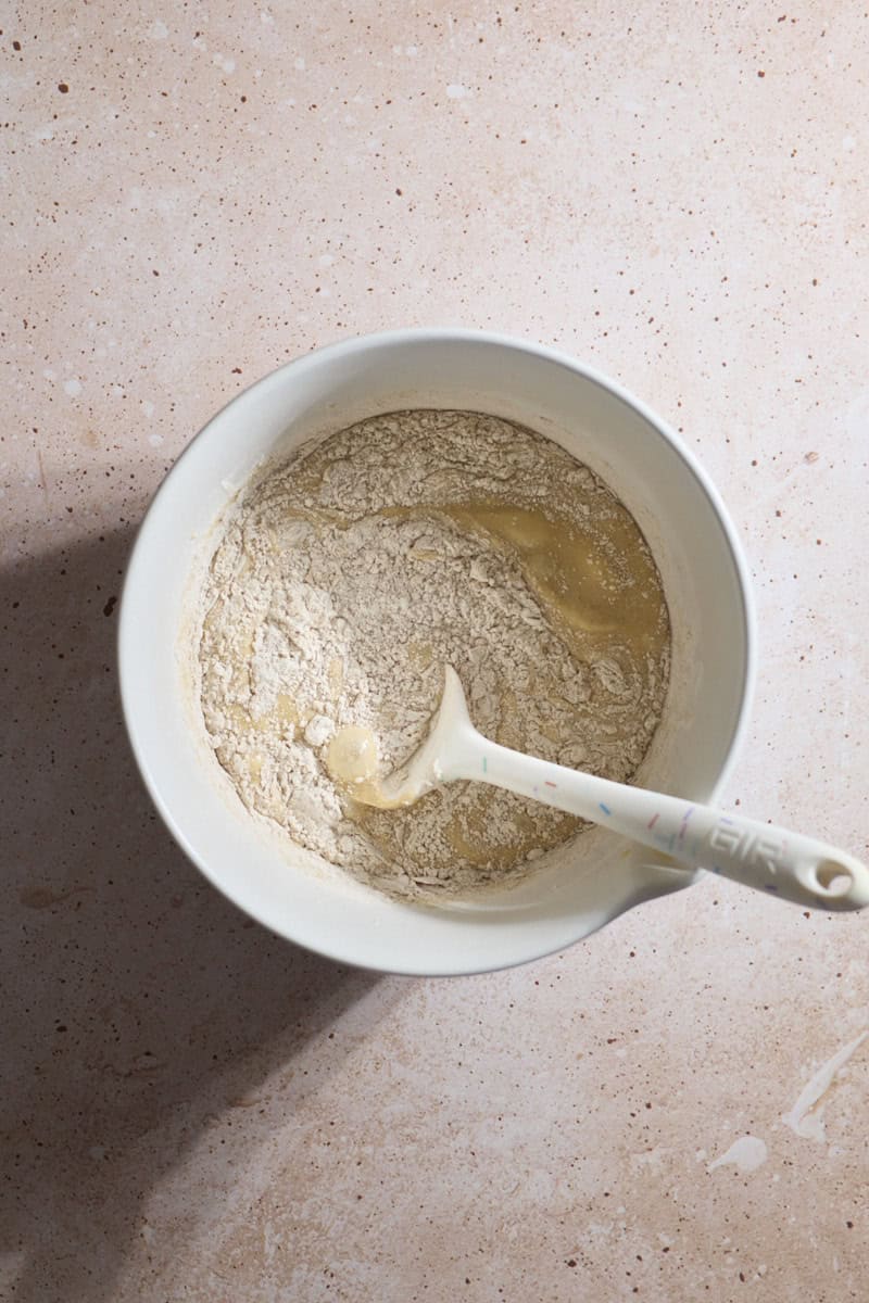 Dry ingredients being mixed into the wet ingredients in a white bowl.