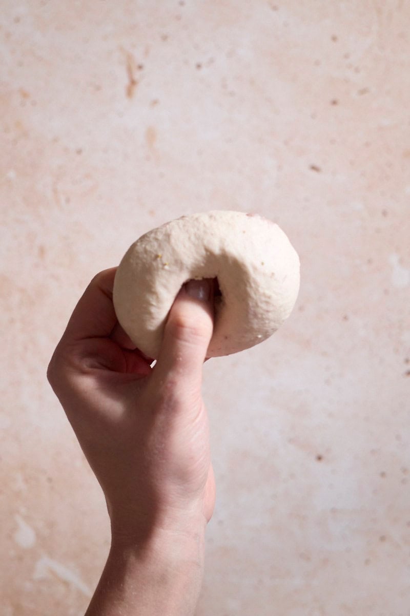 A thumb pressing a hole in the center of the bagel.