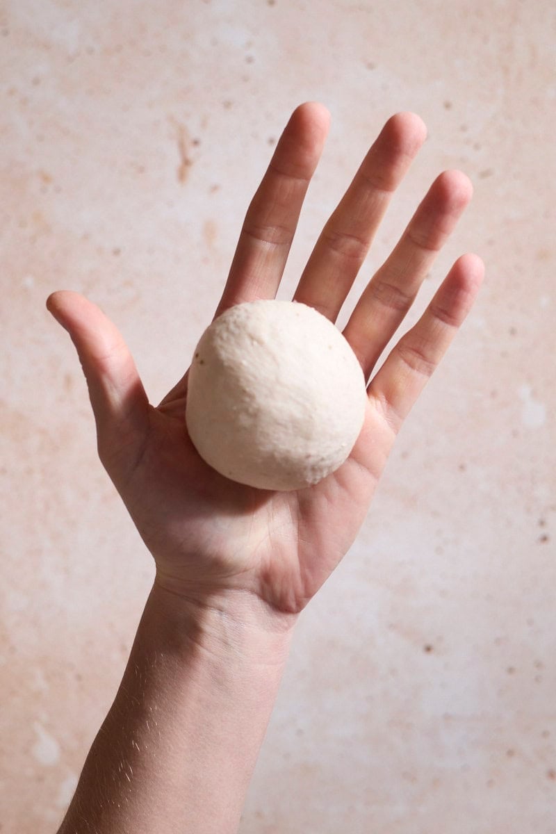 Dough shaped into a ball in the palm of a hand.