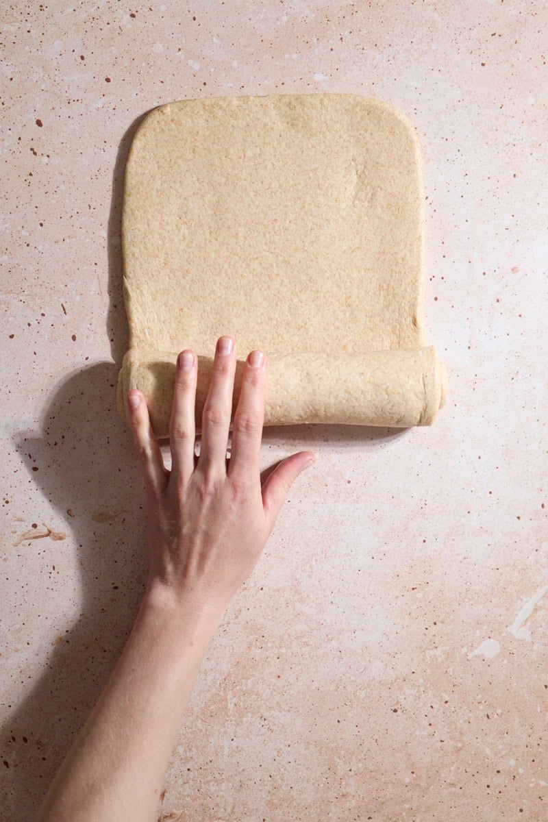 A hand rolling the dough into a log.